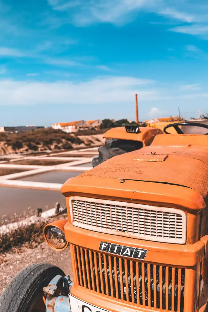 Tracteur orange vintage aux salines de Tavira sous un ciel bleu lumineux.