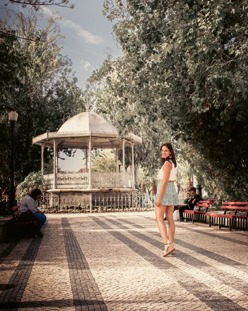 Caroline souriante devant le kiosque romantique du Jardim da Alagoa à Tavira, Algarve, Portugal.
