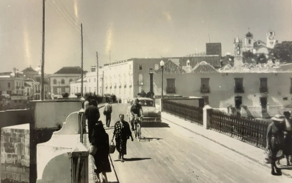 Pont romain de Tavira animé, piétons et voitures traversant, ambiance vintage en noir et blanc.