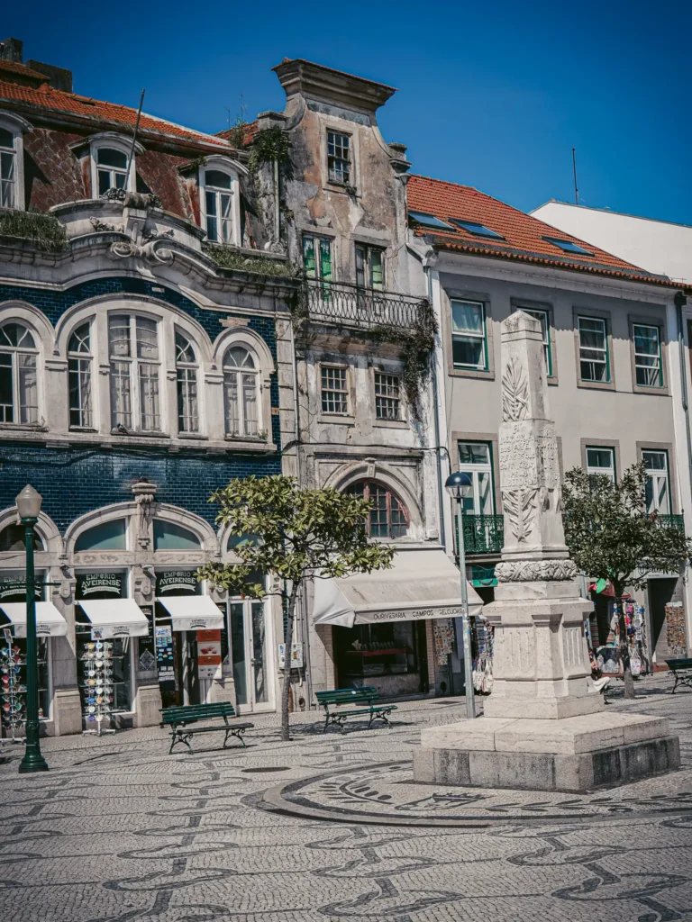 Central square of Aveiro with historic buildings and a stone statue under a blue sky.