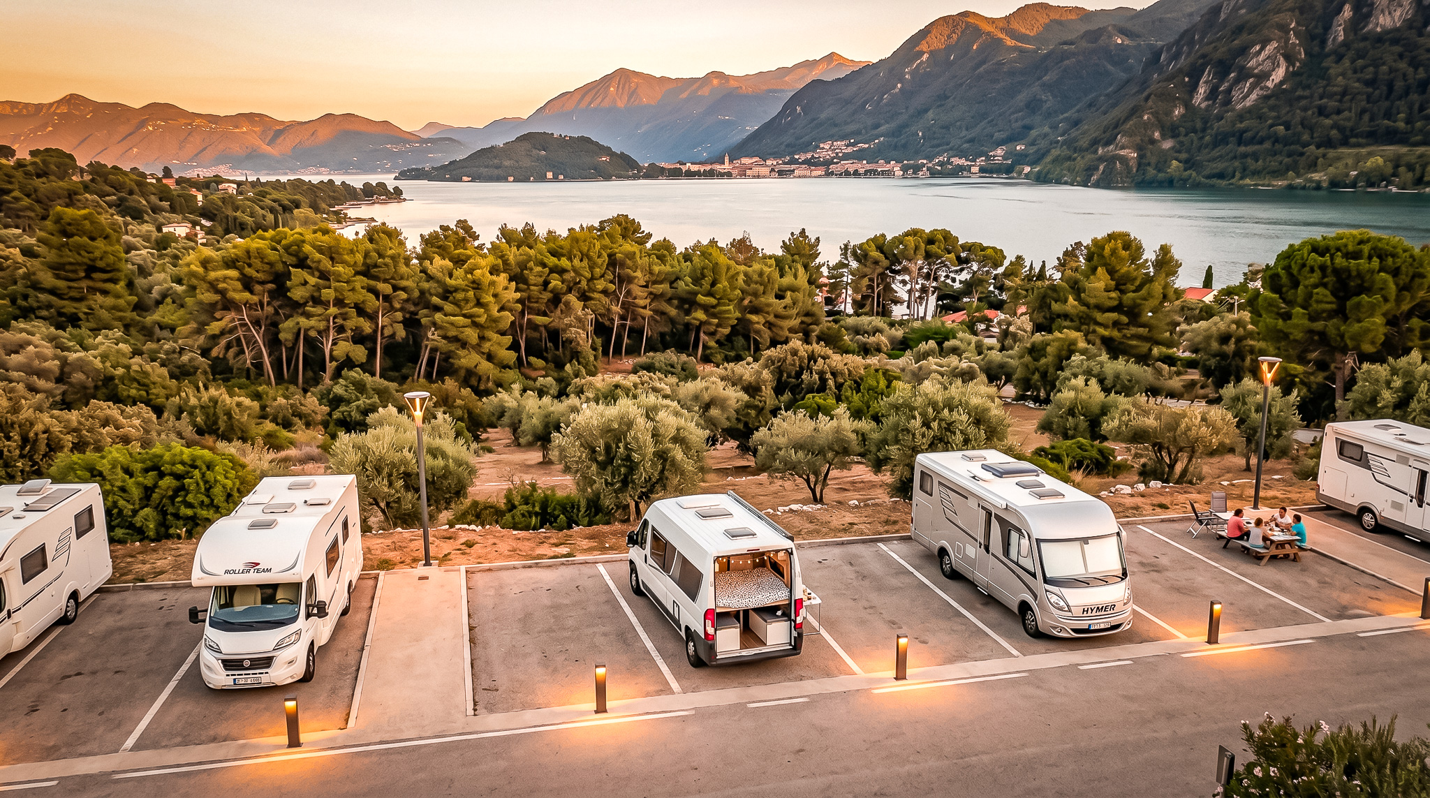 Camper vans parked by Lake Como, mountains in the background, sunset.