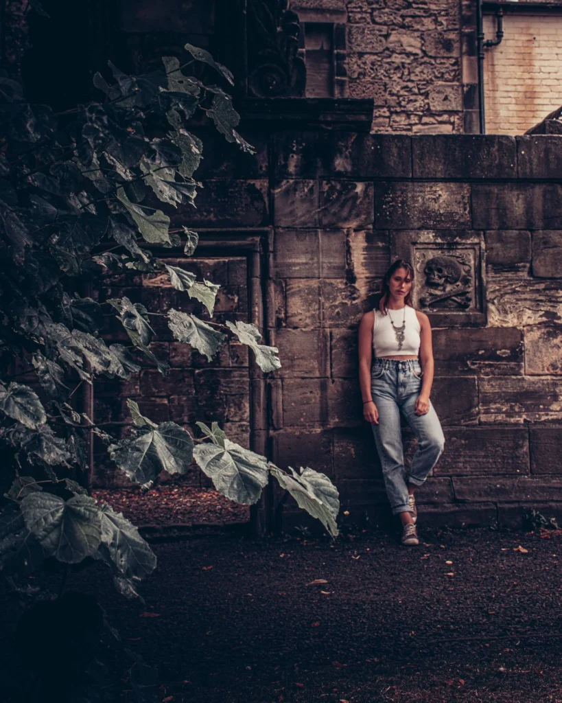 Caroline against an old stone wall adorned with sculptures at Greyfriars cemetery