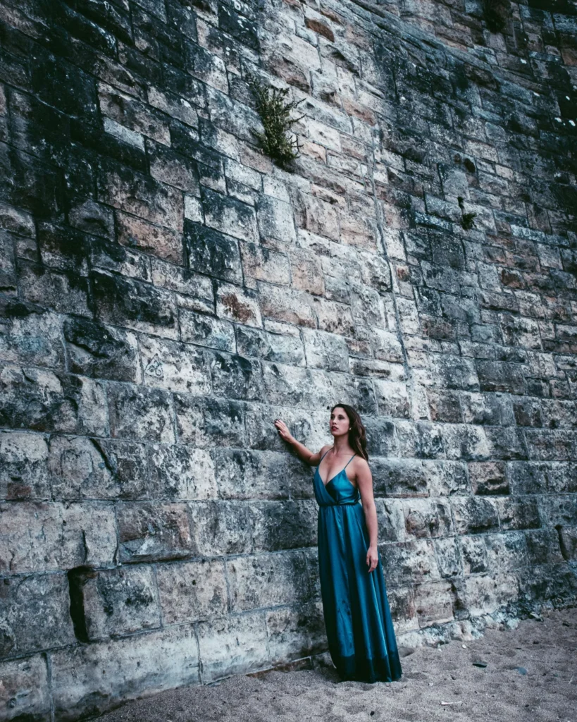 Caroline against a large stone wall on a sandy ground in St Andrews