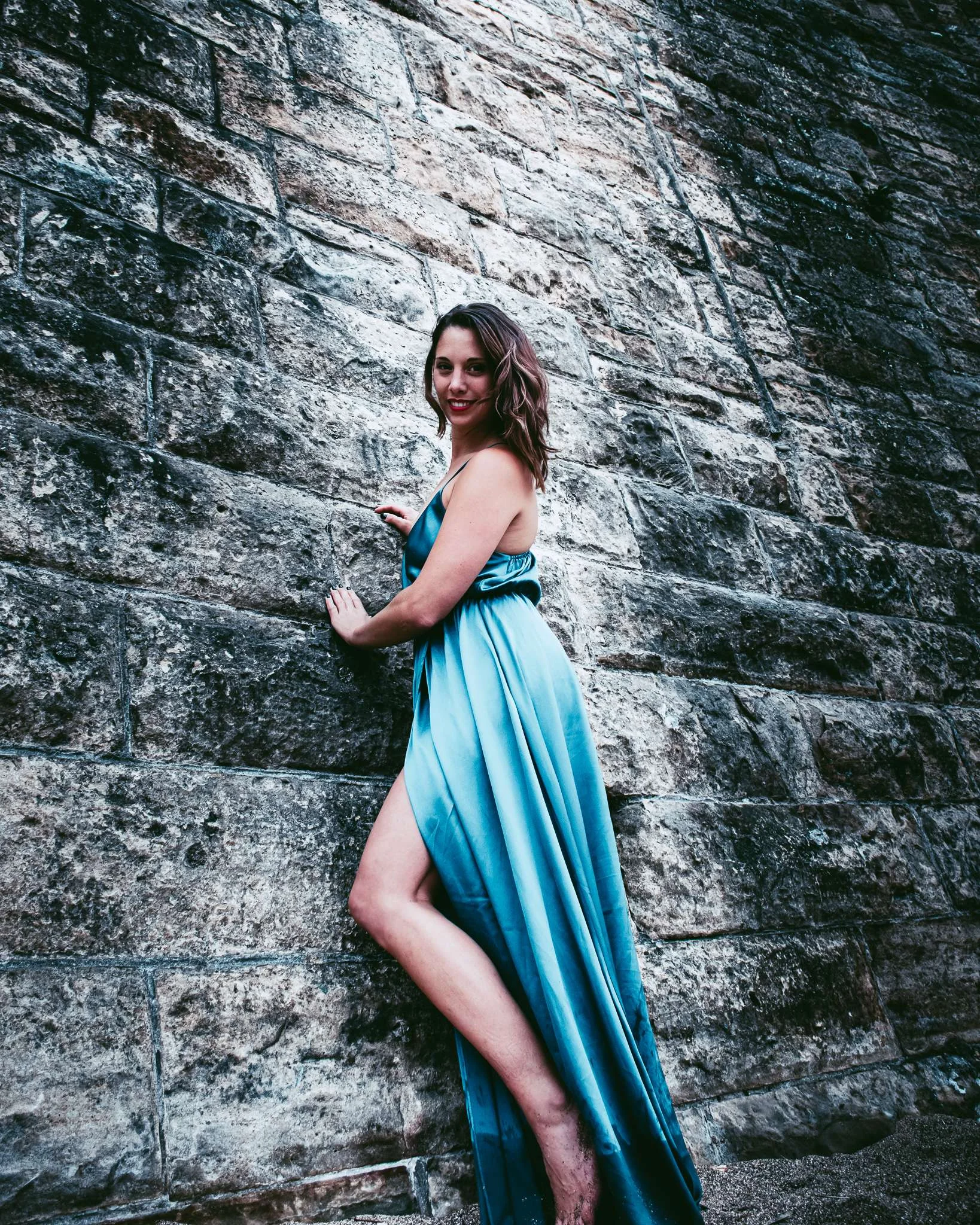 Caroline poses in a long blue dress against a stone wall in St Andrews, Scotland