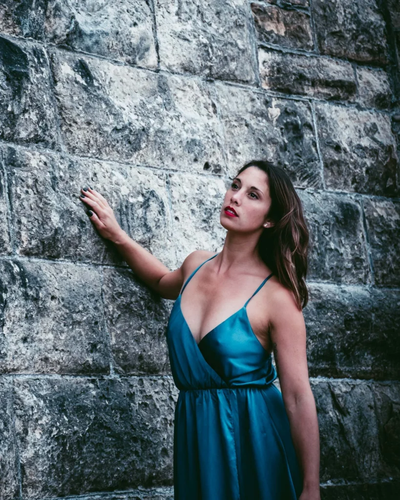 Caroline in a blue satin dress against a stone wall in St Andrews summer 2022