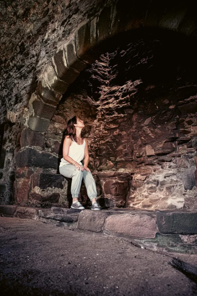 Caroline sitting under a stone arch inside a room of Dunnottar Castle