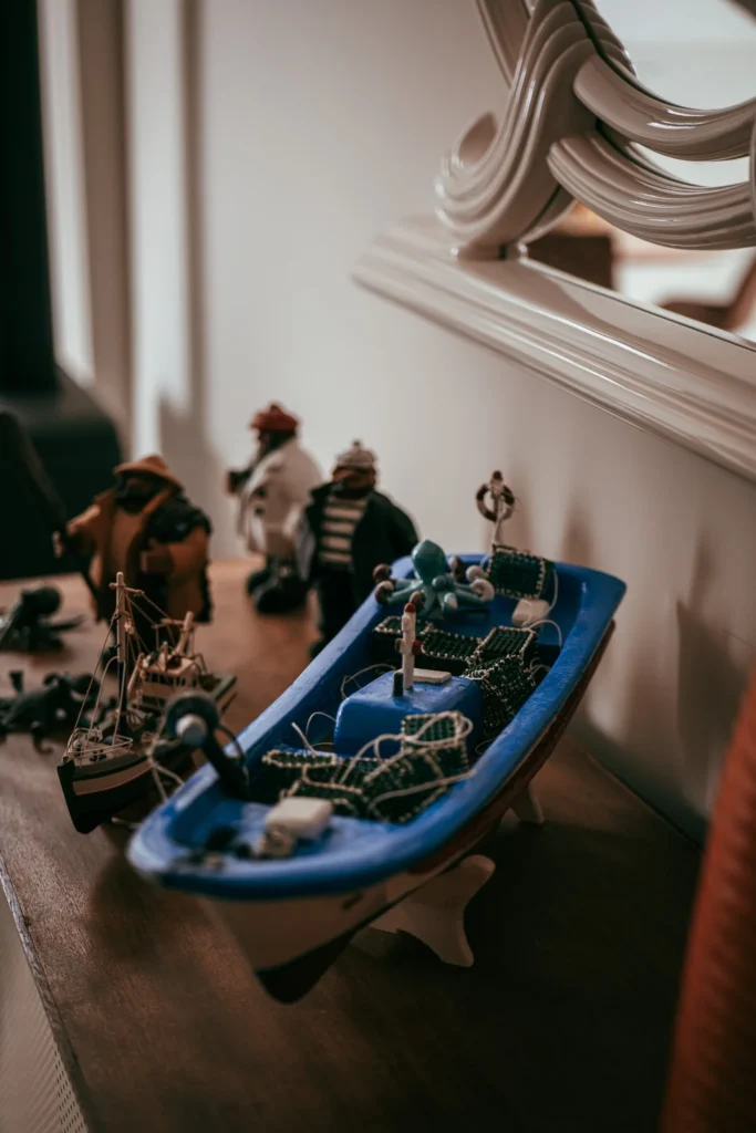 Fishing boat models and sailor figurines displayed on an indoor shelf, decorative ambiance reminiscent of the Portuguese coastline.