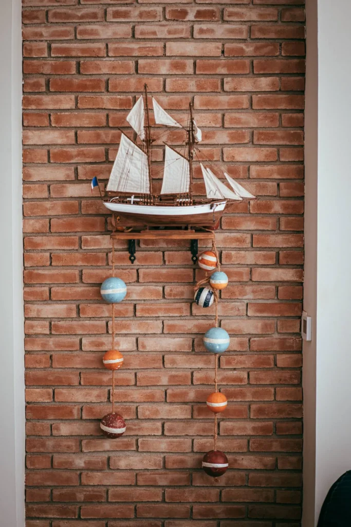 Model of a sailboat hanging on a brick wall, decorated with colorful hanging balls, in an indoor atmosphere in Fuseta, Algarve.
