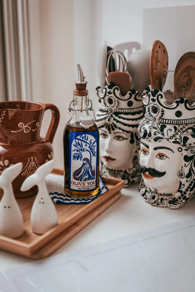 Bottle of 'Olive You' olive oil, decorative pottery, and kitchen utensils on a countertop in Fuseta, Algarve, during the Casita Erika shoot in May 2026.