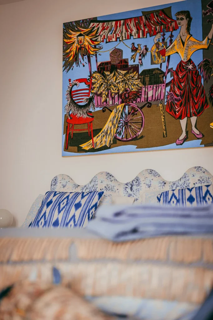 Bed decorated with blue patterned cushions in a room of the Casita Erika in Fuseta, Algarve, with a large colorful artwork hanging on the wall.