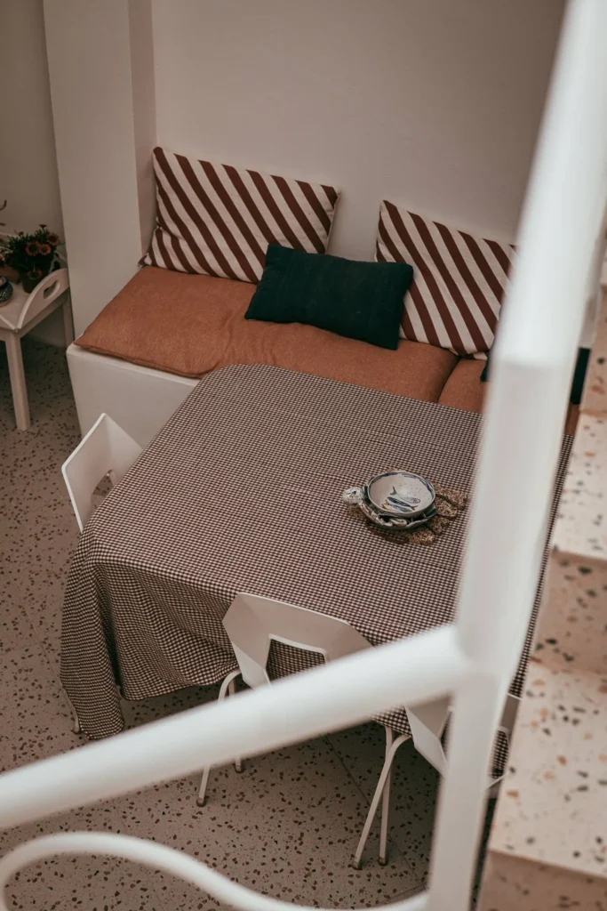Indoor dining area with a table covered in a checkered tablecloth, white chairs, and a bench with striped cushions, photographed during the Casita Erika shoot in Fuseta, Algarve.