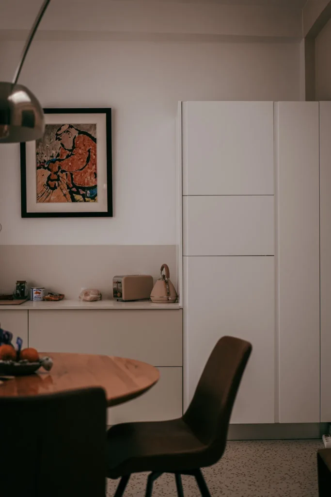 Modern and minimalist kitchen in Fuseta, Algarve, featuring white furniture, a wooden table, and everyday objects on the countertop. A colorful piece of art is hung on the wall.