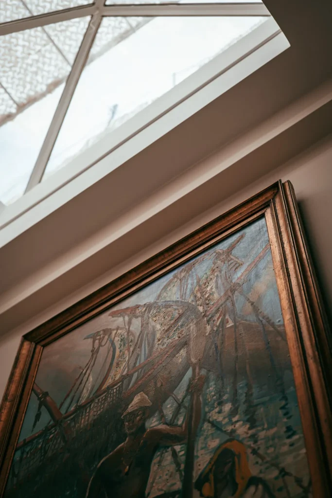 Framed tableau depicting a fishing or sailing scene, photographed under a glass roof in a bright house in Fuseta, Algarve.