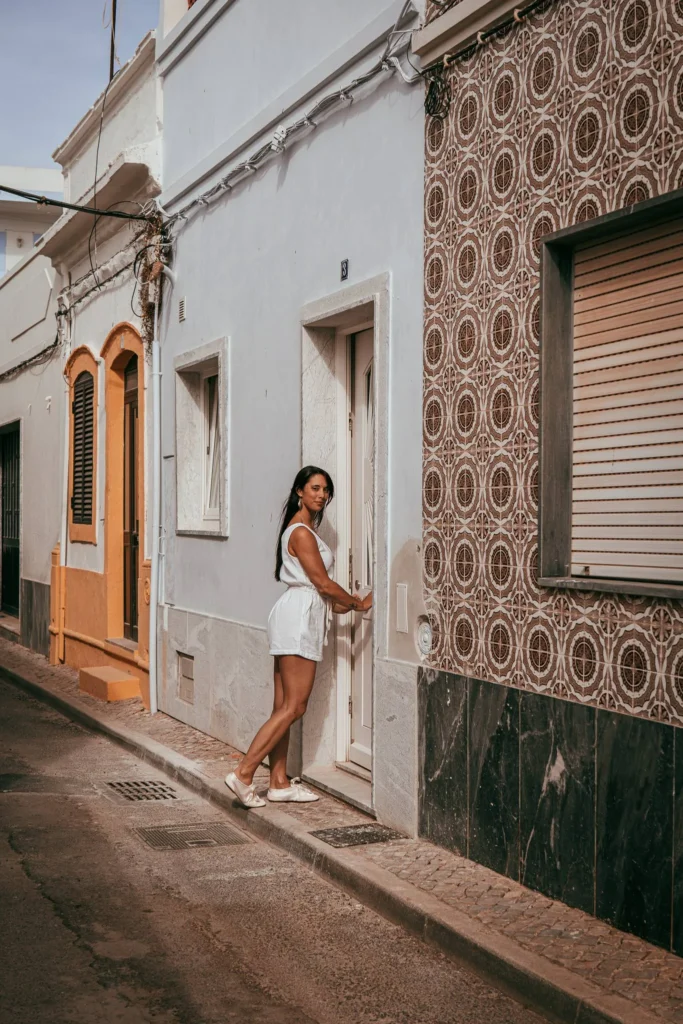 Caroline in front of a typical facade house in a alley in Fuseta, Algarve, during a photoshoot in May 2026.