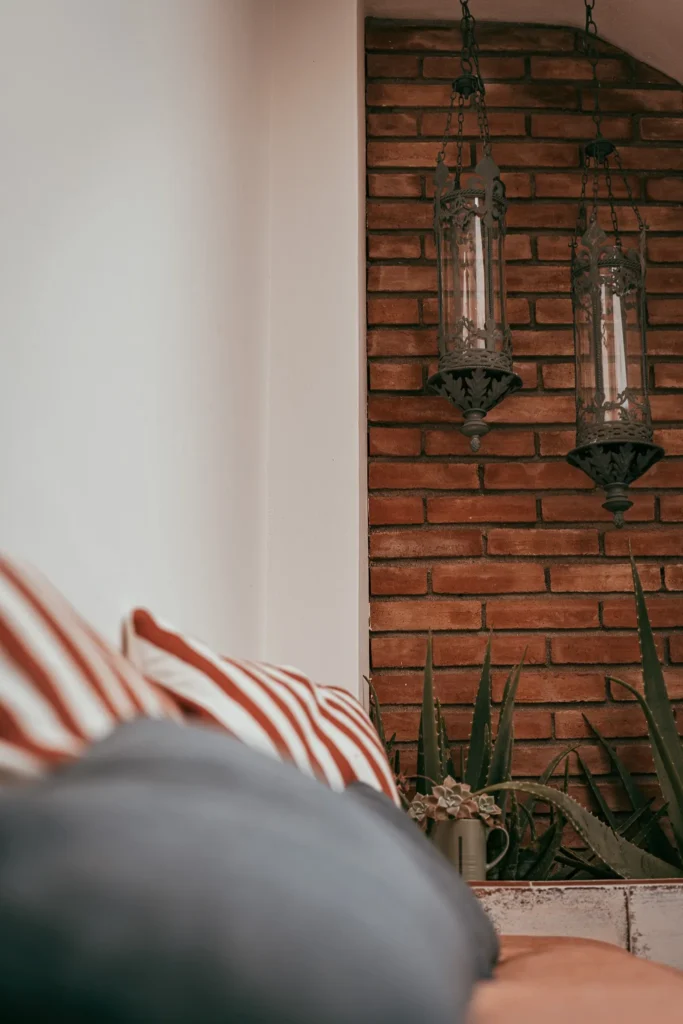 Outdoor lounge area with striped cushions, brick wall, Moroccan lanterns, and plants, warm atmosphere in Fuseta, Algarve.