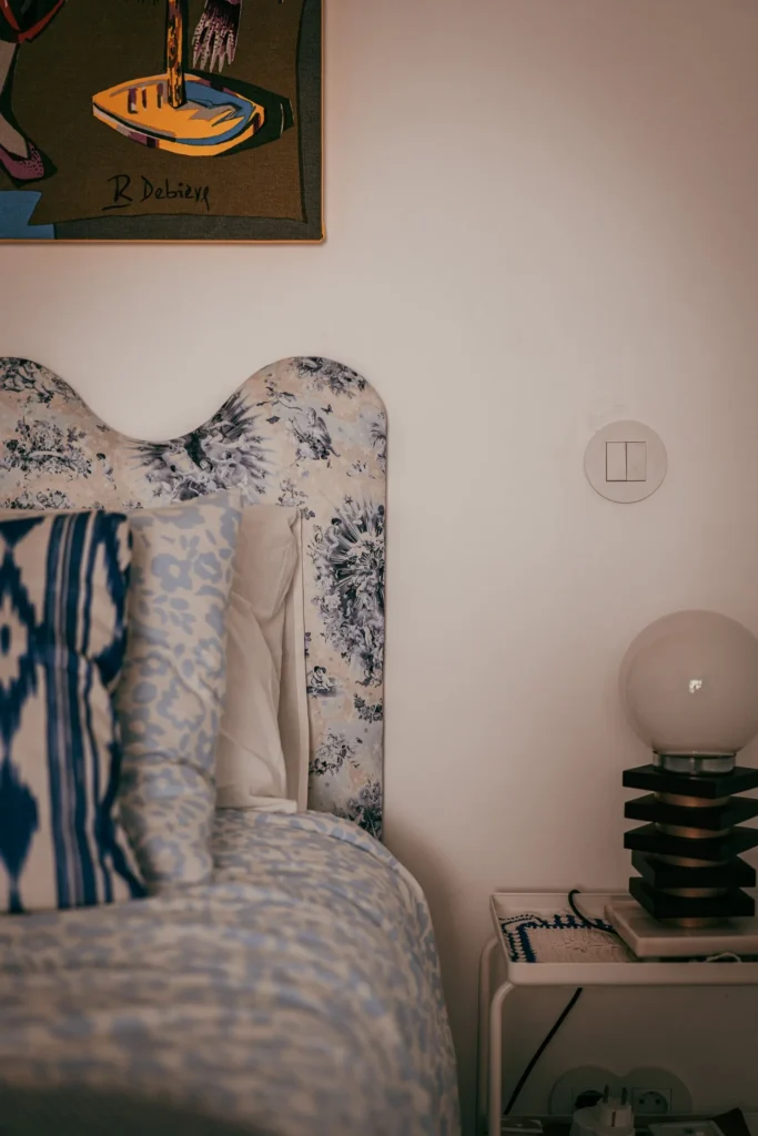 Corner of a room in Fuseta with a floral headboard, a white bedside table, and a designer lamp, soft and contemporary atmosphere.