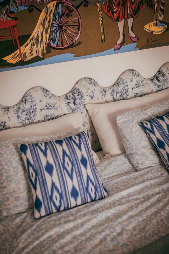 Double bed decorated with blue patterned cushions and a floral headboard, under a colorful tapestry in a room in Fuseta, Algarve.