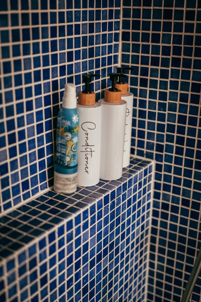 Bottles of skincare products placed on a shelf in a blue-tiled shower during the Casita Erika shoot in Fuseta, Algarve.