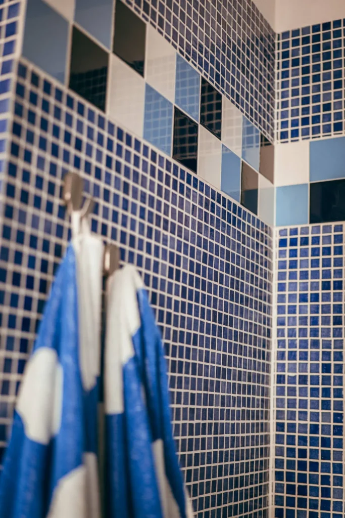 Detail of a bathroom wall with blue and white mosaic tiles, two towels hanging in the foreground. Typical Mediterranean atmosphere of a holiday home in Portugal.