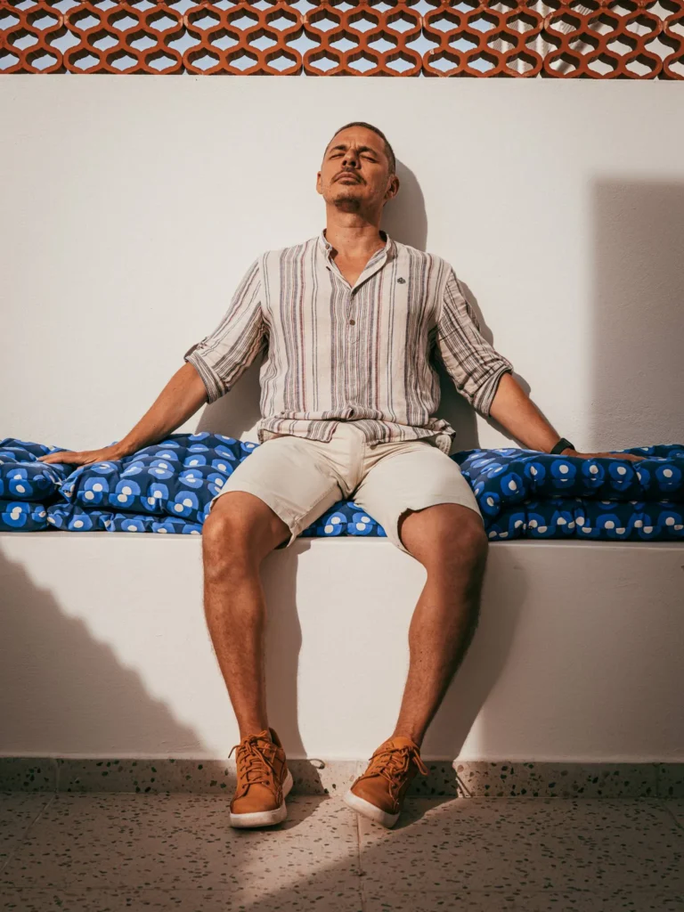 Xavier sitting on a white outdoor bench, enjoying the sun in Fuseta in the Algarve, with a blue patterned cushion underneath him.