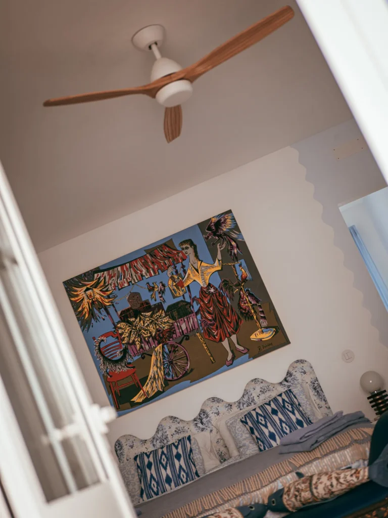 Room decorated with a blue patterned bed, a ceiling fan, and a large colorful painting hanging on the wall, in a house in Fuseta, Algarve.