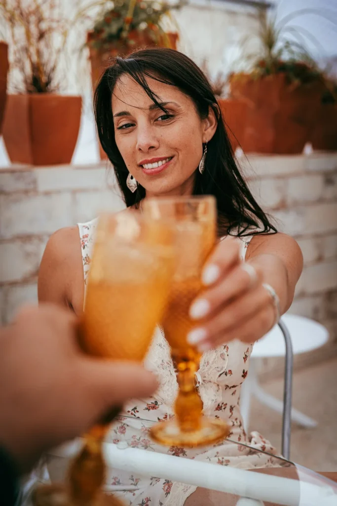 Caroline sitting on the terrace in Fuseta, Algarve, toasts with an amber drink during the Casita Erika shoot in May 2026.