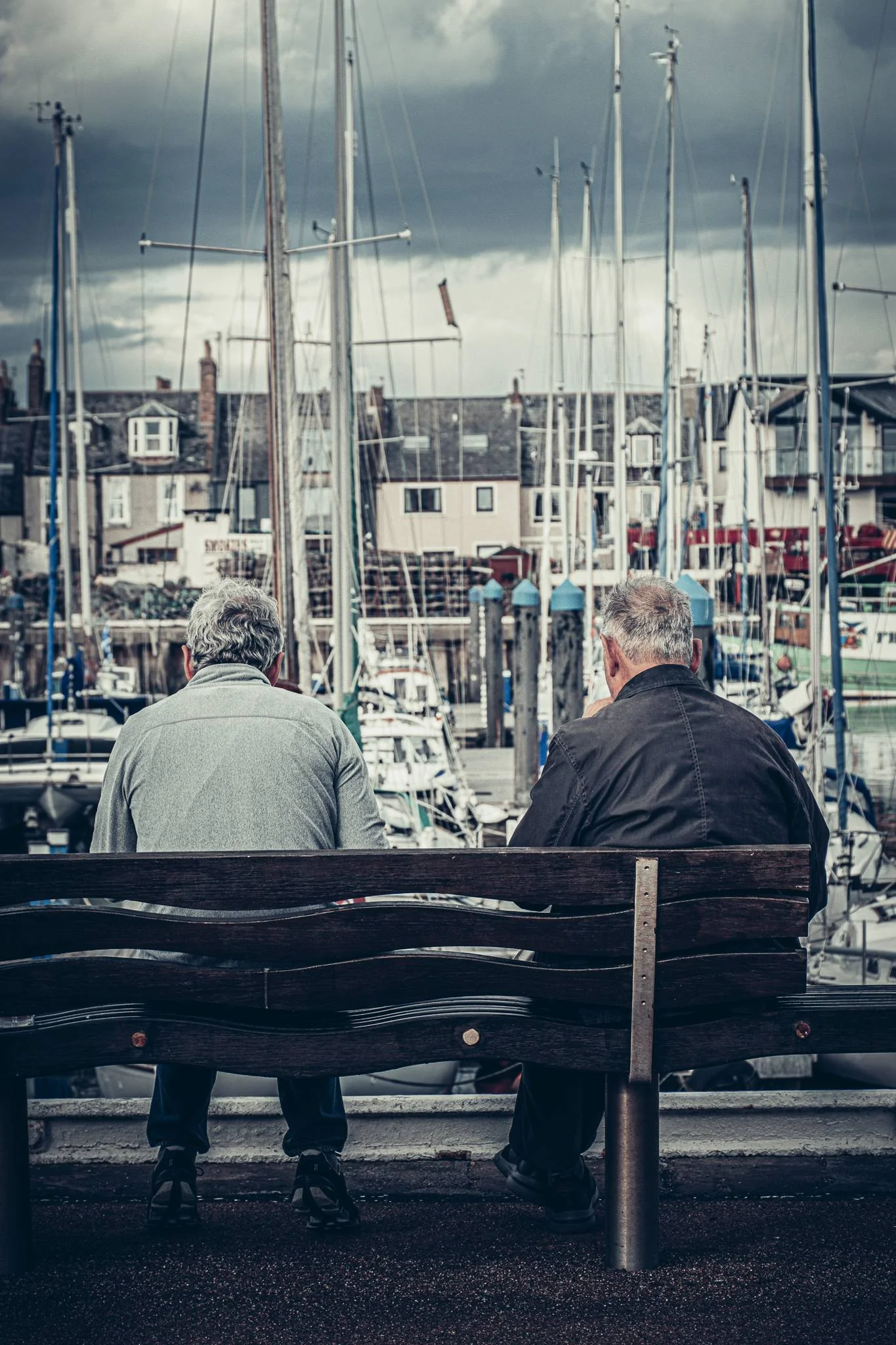 Two men sitting on a bench facing the marina of Arbroath in Scotland