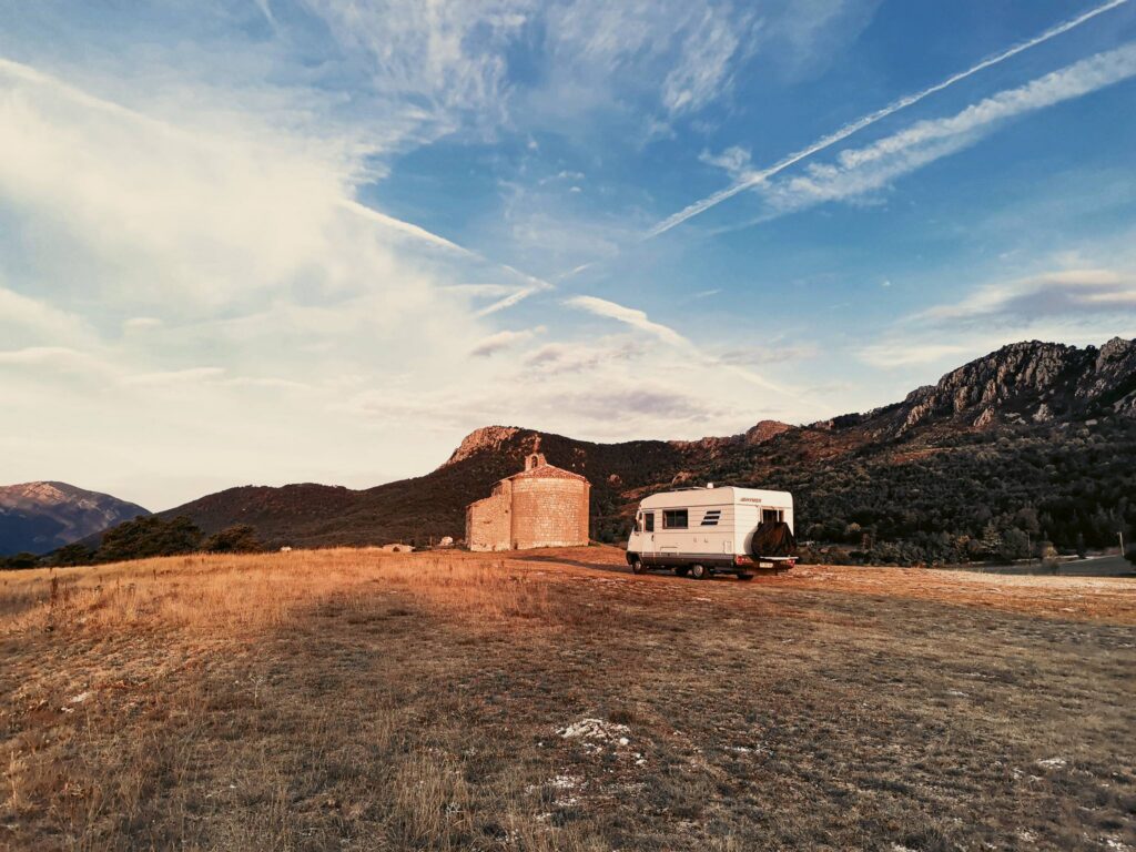 Camper Edouard is parked in front of a stone chapel surrounded by mountains, symbolizing the mobility and fiscal flexibility of the nomad.