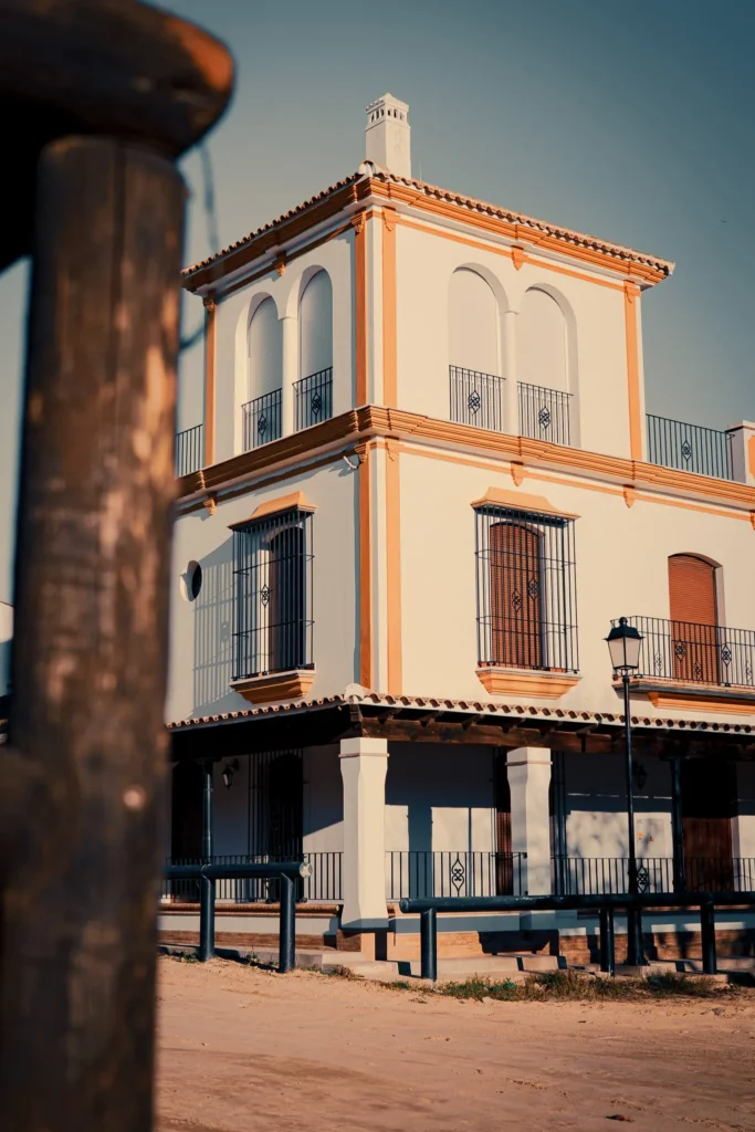 Traditional Andalusian building with a white and ochre facade, photographed under a clear sky in El Rocio, Andalusia.