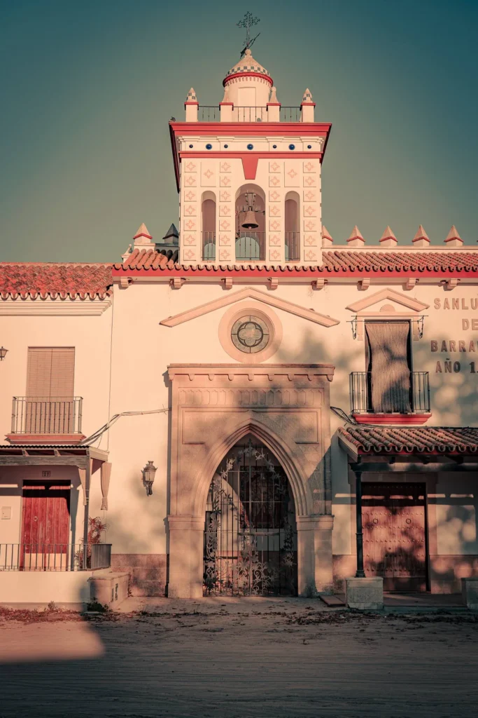 Facade of a typical religious building in Andalusia at El Rocio, featuring traditional architecture and a bell tower topped with a cross, under the soft light of the late afternoon.