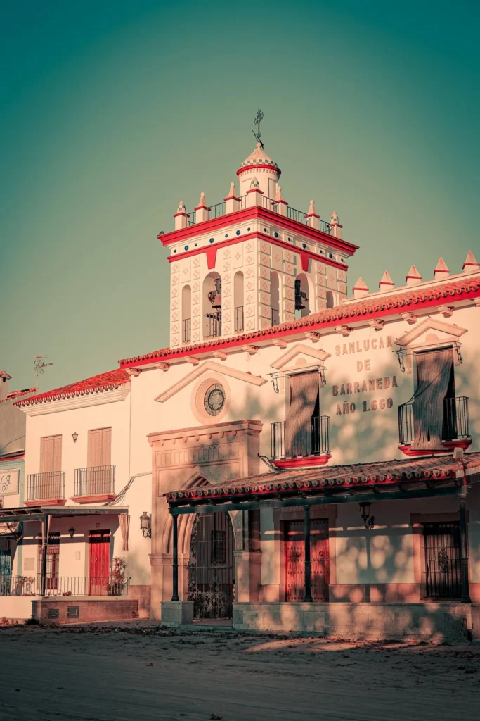 Facade of a traditional Andalusian building in El Rocio, illuminated by golden light at the end of the day, featuring an ornate tower and wall inscriptions.
