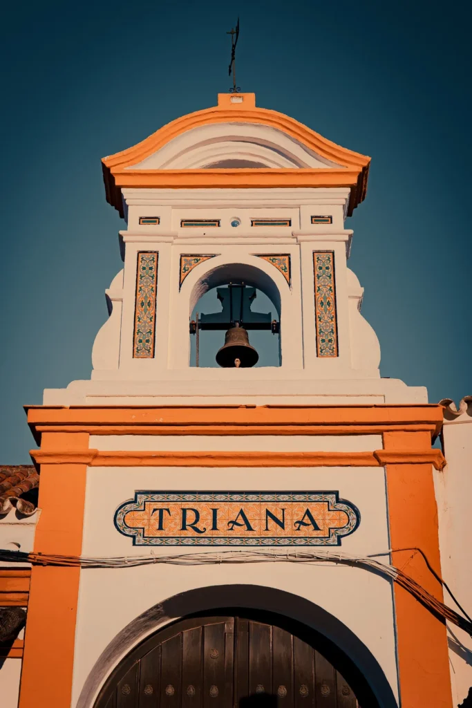 Facade of an Andalusian chapel in El Rocio, adorned with colorful ceramics and a bell, under a clear sky in winter.