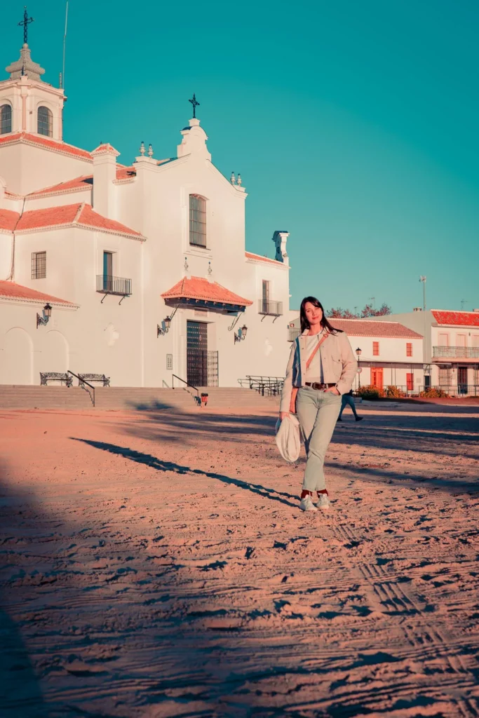 Caroline walks on the sand in front of the white sanctuary of El Rocio in Andalusia, under a clear winter sky.
