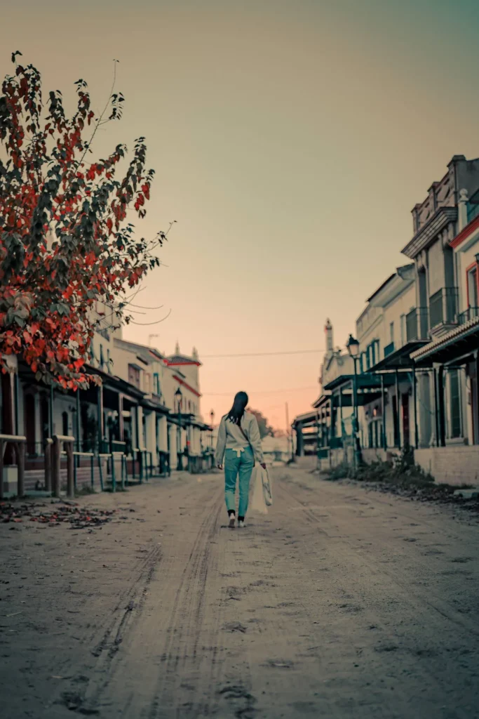 Caroline walks alone down a sandy street lined with traditional houses in El Rocio, Andalusia, at sunset.