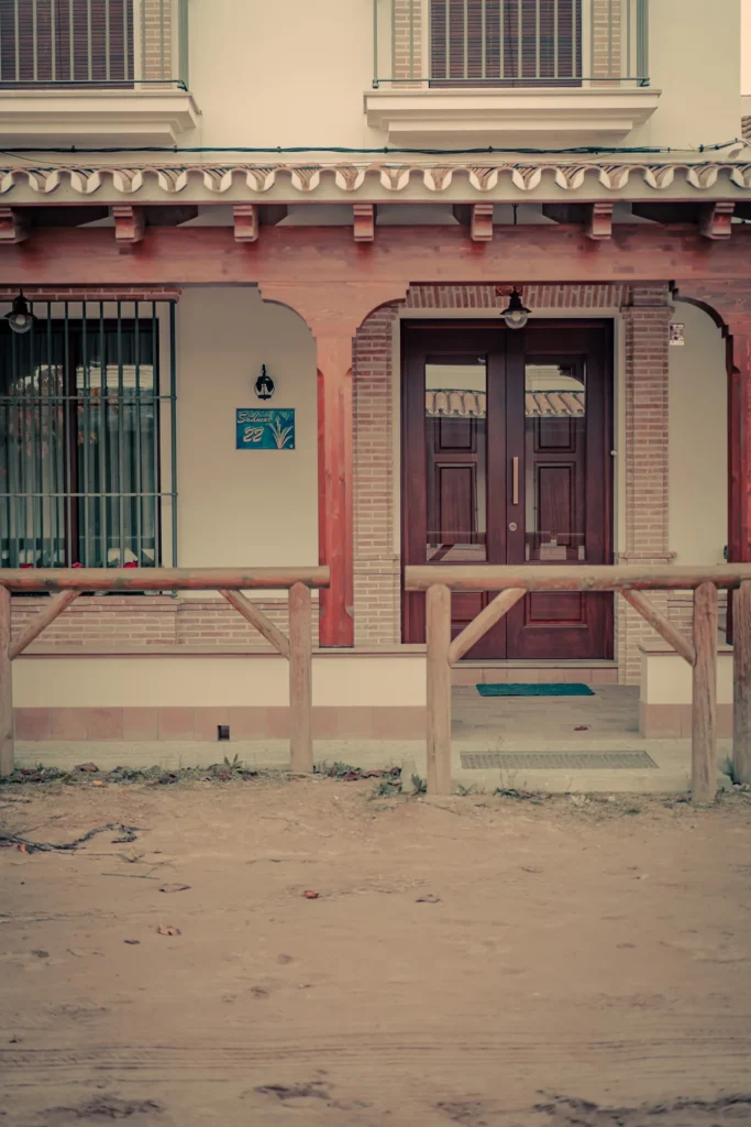 Facade of an Andalusian house in El Rocio with a wooden door, a wooden fence, and a number plate on the wall. The atmosphere is calm and rural in winter.