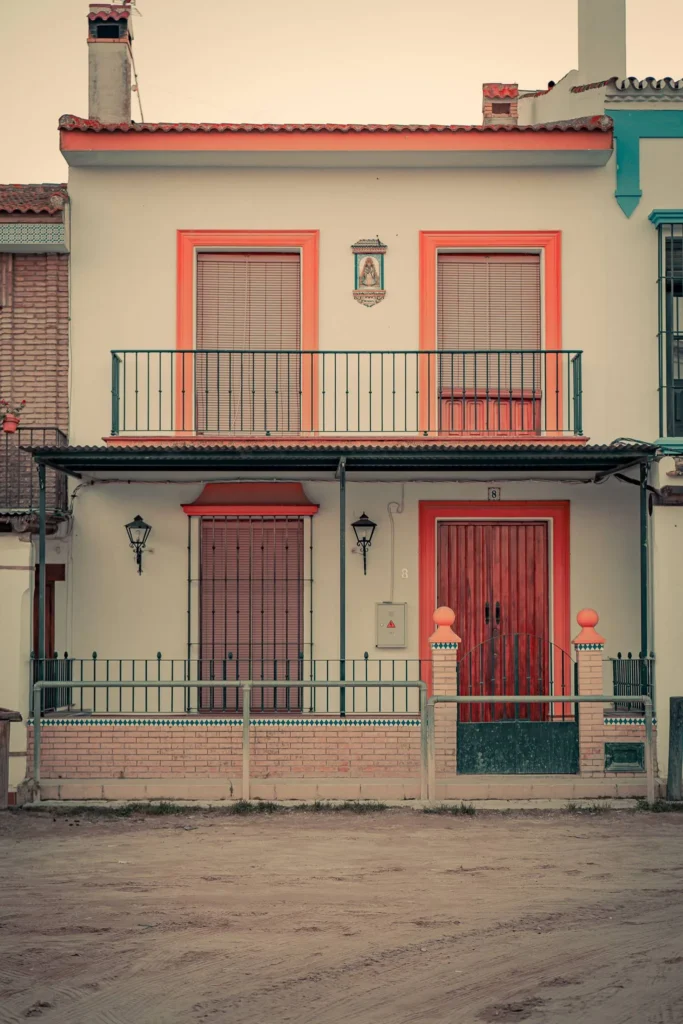 Facade of a typical Andalusian house in El Rocio, with closed shutters, orange frames, and religious decoration above the balcony.