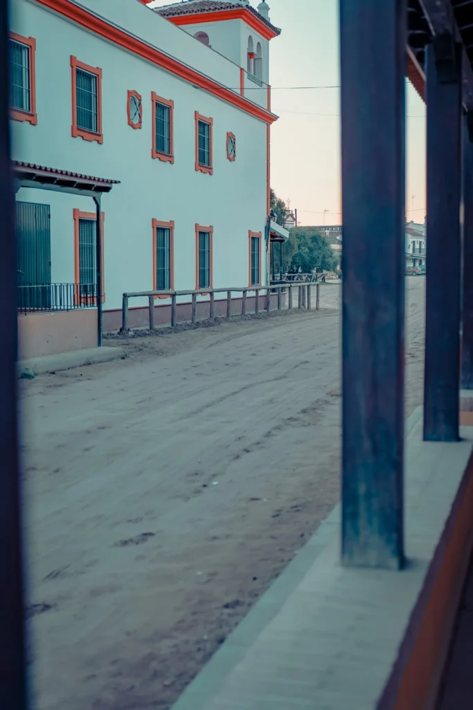 Deserted street lined with a white building with orange frames, typical of Andalusian architecture in El Rocio during winter.