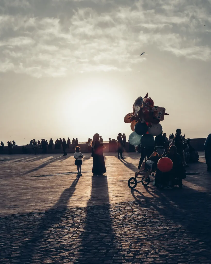 Sunset over the ramparts of Essaouira, crowds strolling with colorful balloons.