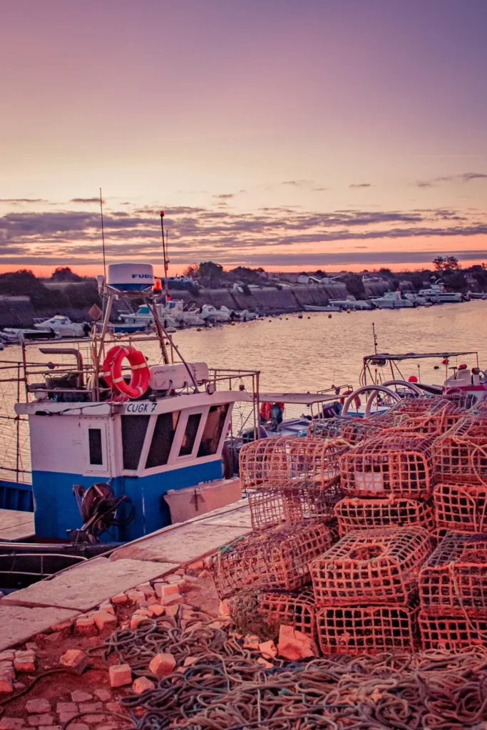 Bateau de pêche amarré au port de Fuseta en Algarve au coucher du soleil, avec des casiers à crustacés empilés sur le quai.