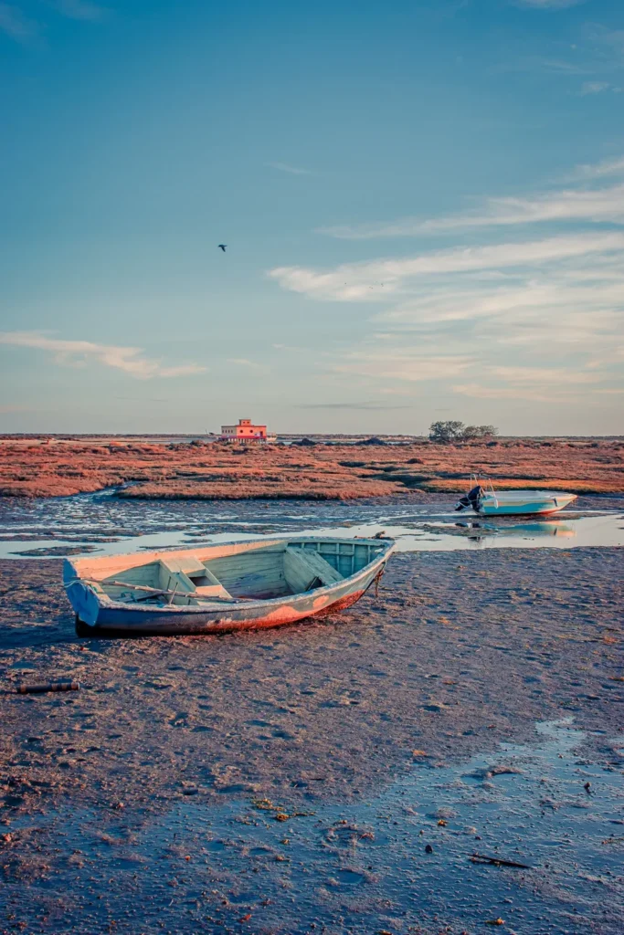 Deux barques échouées sur la vase à marée basse, avec une maison blanche et rouge en arrière-plan sous un ciel dégagé à Fuseta dans l'Algarve, Portugal, en novembre 2022.