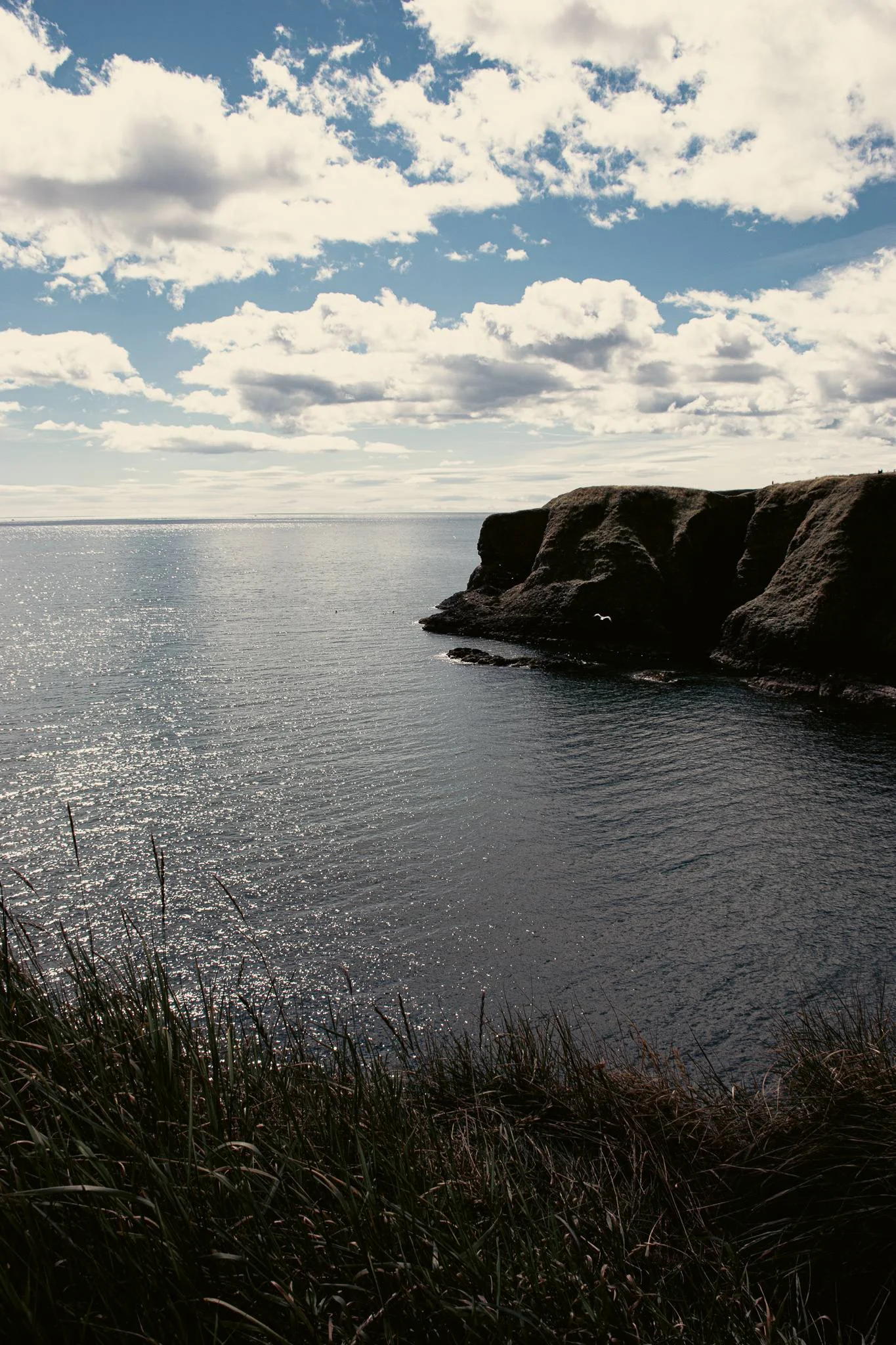 View of the sea and the cliffs of Dunnottar in Scotland under a partly cloudy sky