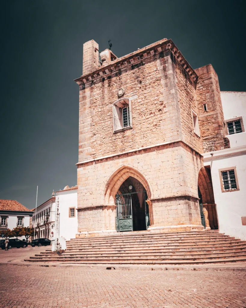 Façade d'un bâtiment historique en pierre avec un portail gothique et des escaliers, sous un ciel dégagé à Faro en Algarve, Portugal, en novembre 2022.