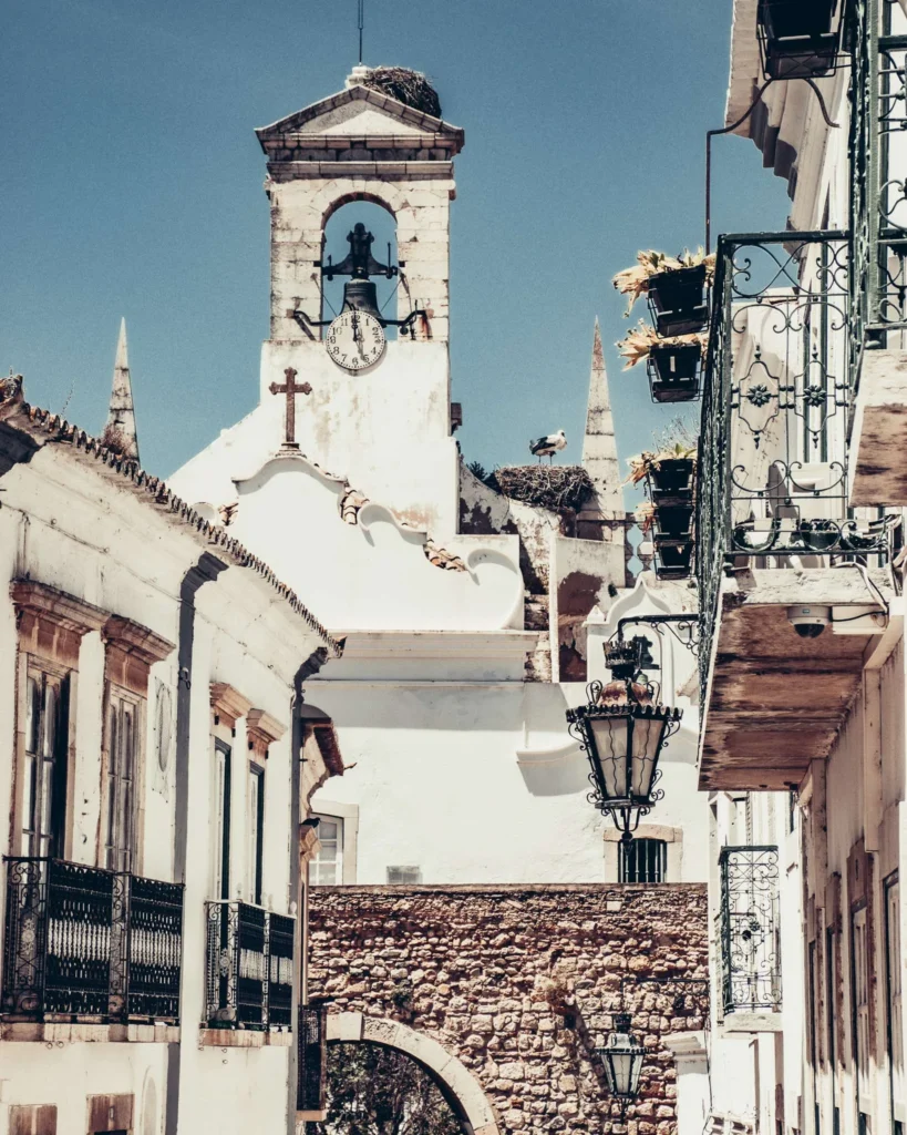 Rue pittoresque du centre historique de Faro avec une église blanche, un clocher et des balcons fleuris sous un ciel bleu, en Algarve au Portugal en novembre 2022.