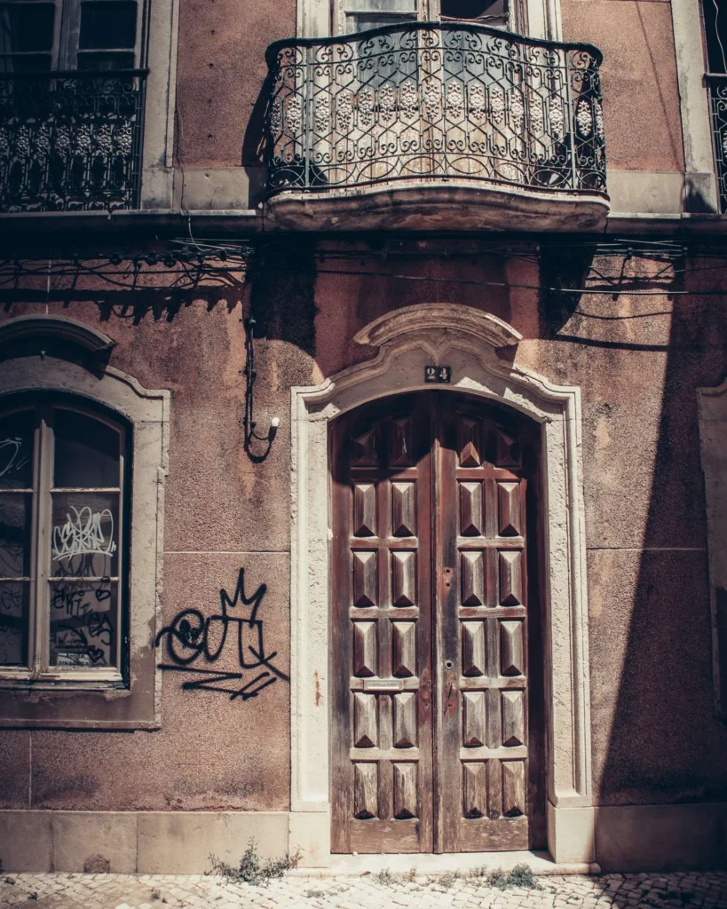 Façade d'un immeuble ancien à Faro avec une porte en bois, un balcon en fer forgé et des graffitis sur le mur. L'ambiance rappelle l'architecture traditionnelle de l'Algarve au Portugal en automne.