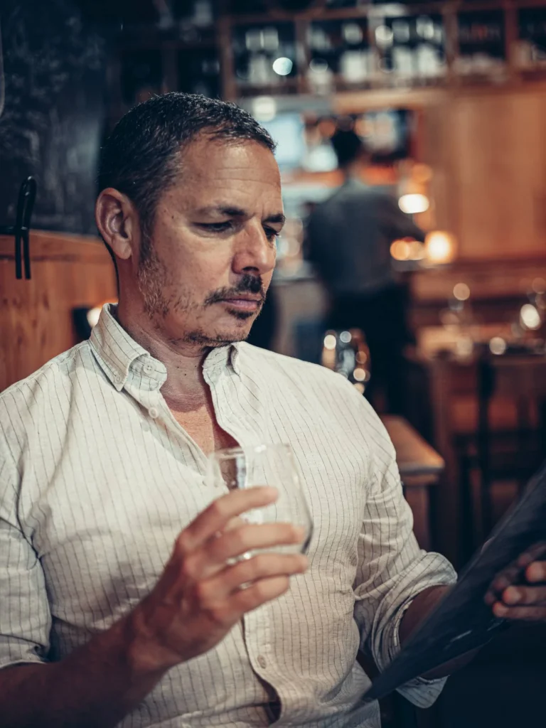 Xavier sitzt in einem Restaurant in Faro, hält ein Glas und schaut in die Speisekarte bei einer gemütlichen Atmosphäre.