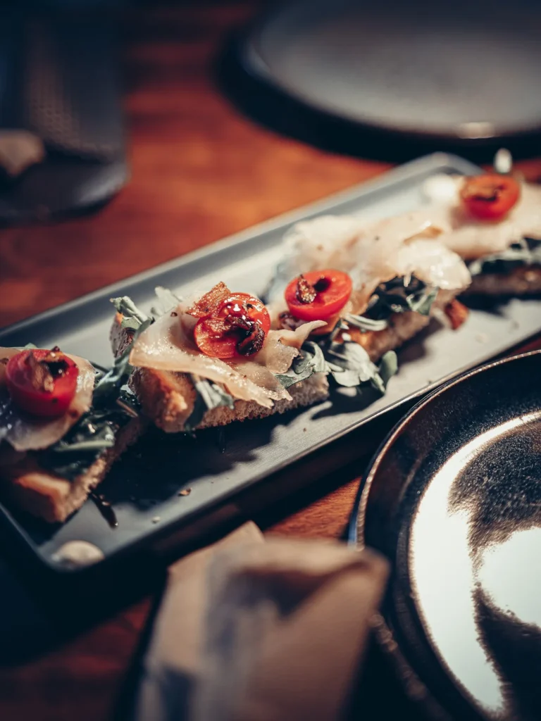 Tapas-Teller bestehend aus belegten Broten mit frischem Gemüse und geräuchertem Kabeljau, serviert auf einem Holztisch im Restaurant 8 Tapas in Faro, Algarve.