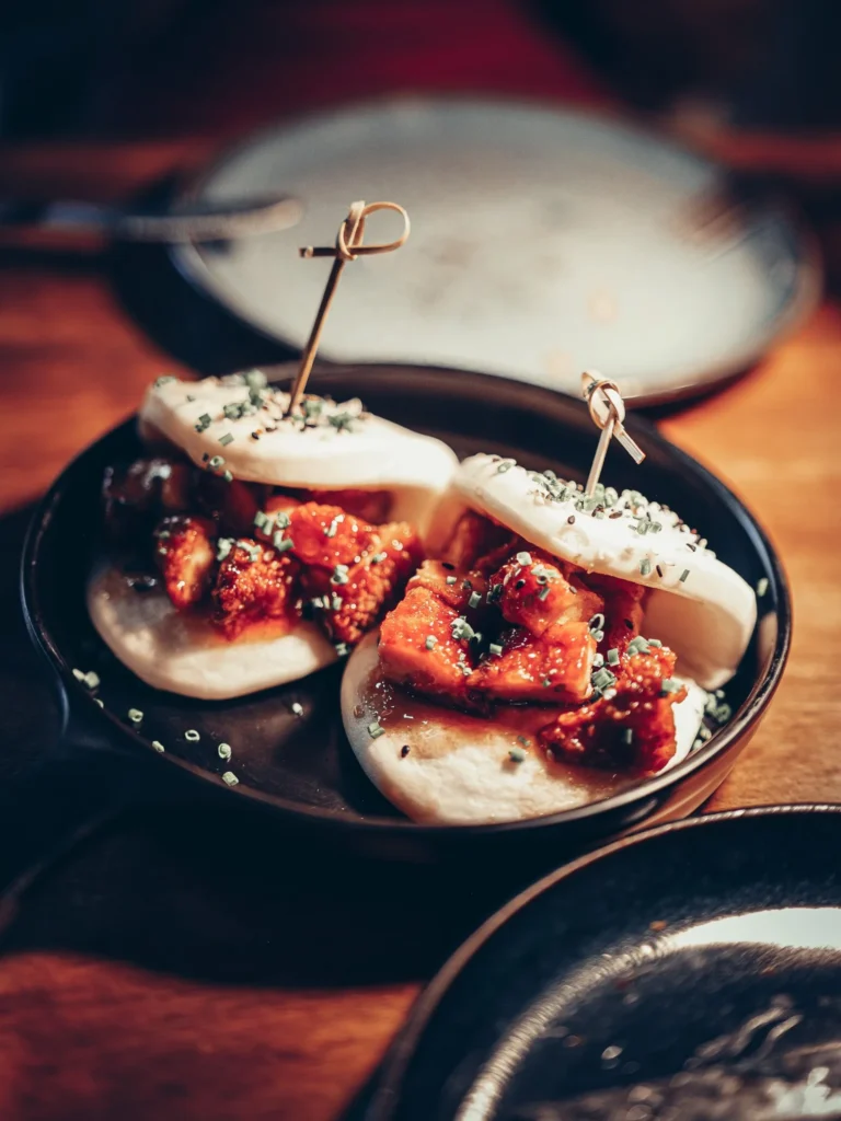 Bao-Teller gefüllt mit knusprigen Hähnchenstücken und Schnittlauch, serviert auf einem Holztisch im Restaurant 8 Tapas in Faro, Algarve.