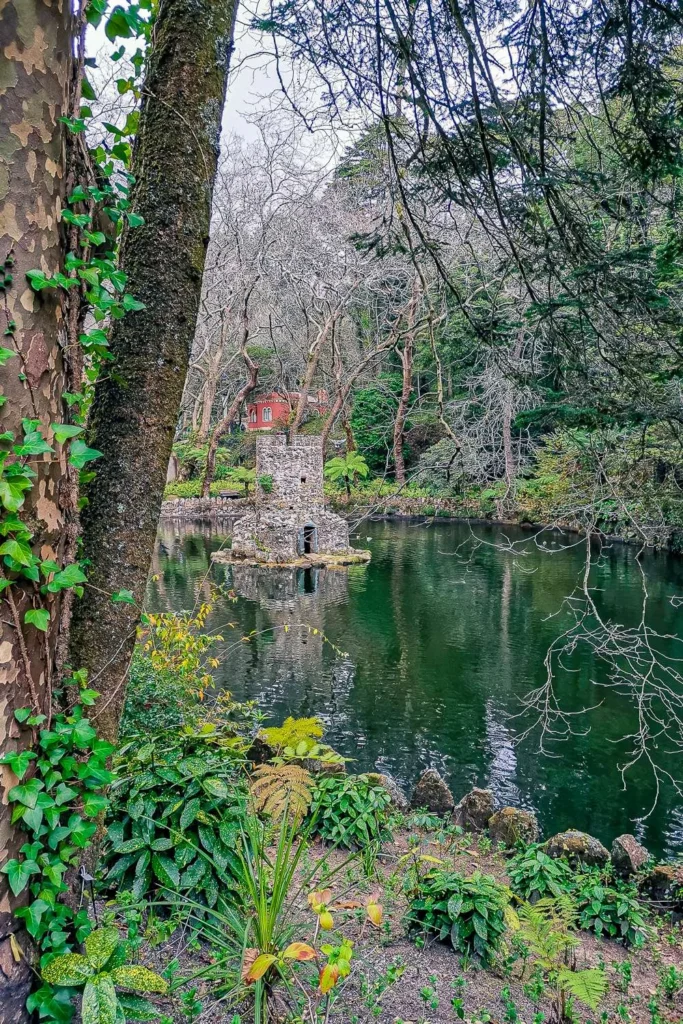 View of a small stone pavilion in the center of a pond surrounded by dense vegetation in the park of the National Palace of Pena, in Portugal, in winter.