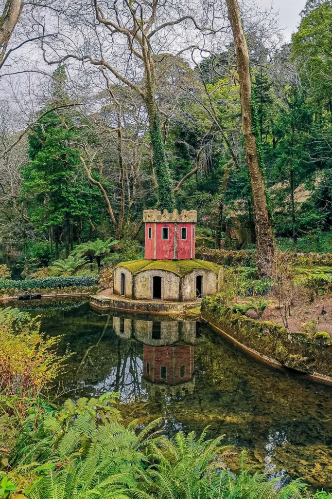 A small colorful pavilion surrounded by a pond and lush vegetation in the park of the National Palace of Pena, in Portugal, during winter.