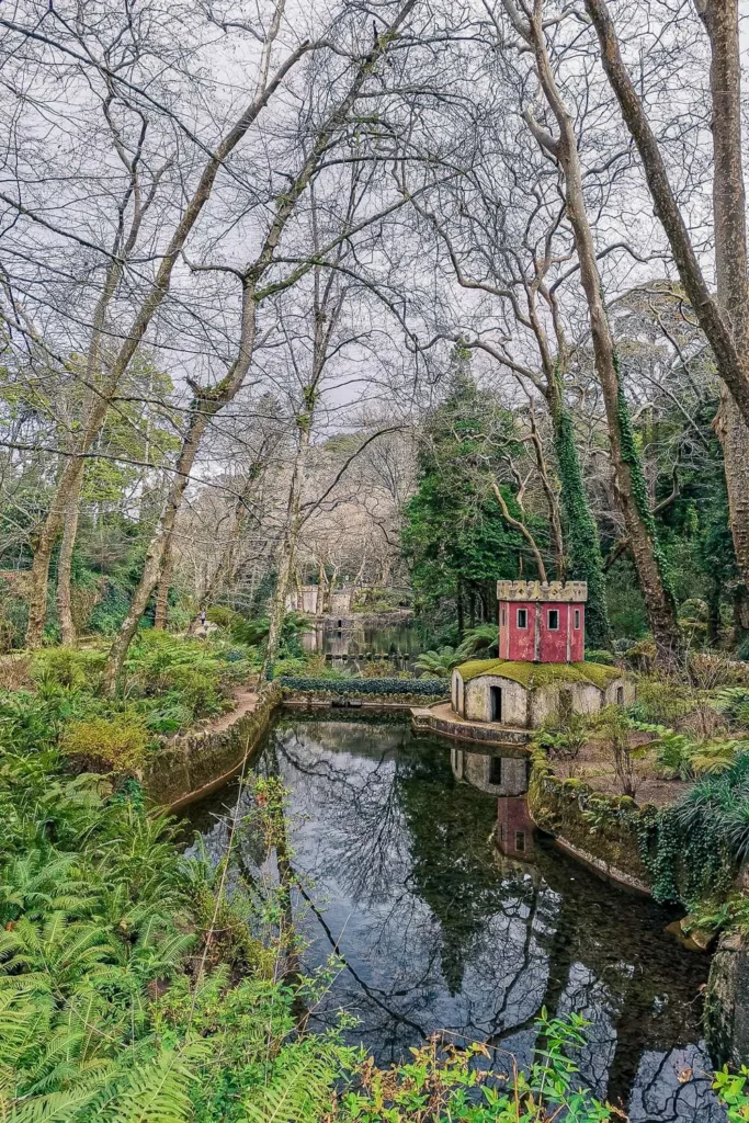 National Palace of Pena Garden in Portugal, with a small red pavilion by a pond surrounded by trees in winter.